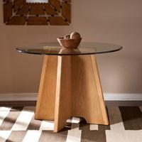 Update your breakfast or dinner area with this Art Deco inspired round table. Match your favorite chairs to this casual dining pedestal table to create a unique look that's contemporary and eclectic. Interlocking panels form an architectural design in a tapered frame. Wood grain details add tone and texture with a natural oak finish. The clear tempered glass top with a sleek bevel extends past the base for a floating edge that is refined and easy to clean. - Comfortably seats 2-4 people - Durable tempered glass - Versatile for matching your favorite chairs - Contemporary casual dining with wood grain details - Natural oak finish with beveled glass - Tabletop: 40.25" DIA - Glass: 41.75" DIA - Chair/leg room: 28.25" W x 19.75" D x 30.25" H (triangular) - Clearance: 9" W x 2.5" H - Approx. weight: 130.5 lb. - Supports up to: 60 lb. - Materials: solid wood, MDF, ash veneer, 12mm tempered glass with .75" bevel, aluminum - Assembly required - Overall: 41.75" DIA x 30.75" H