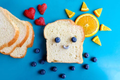 Free Fun and colorful toast face art with blueberries, strawberries, and orange slices on a blue background. Stock Photo